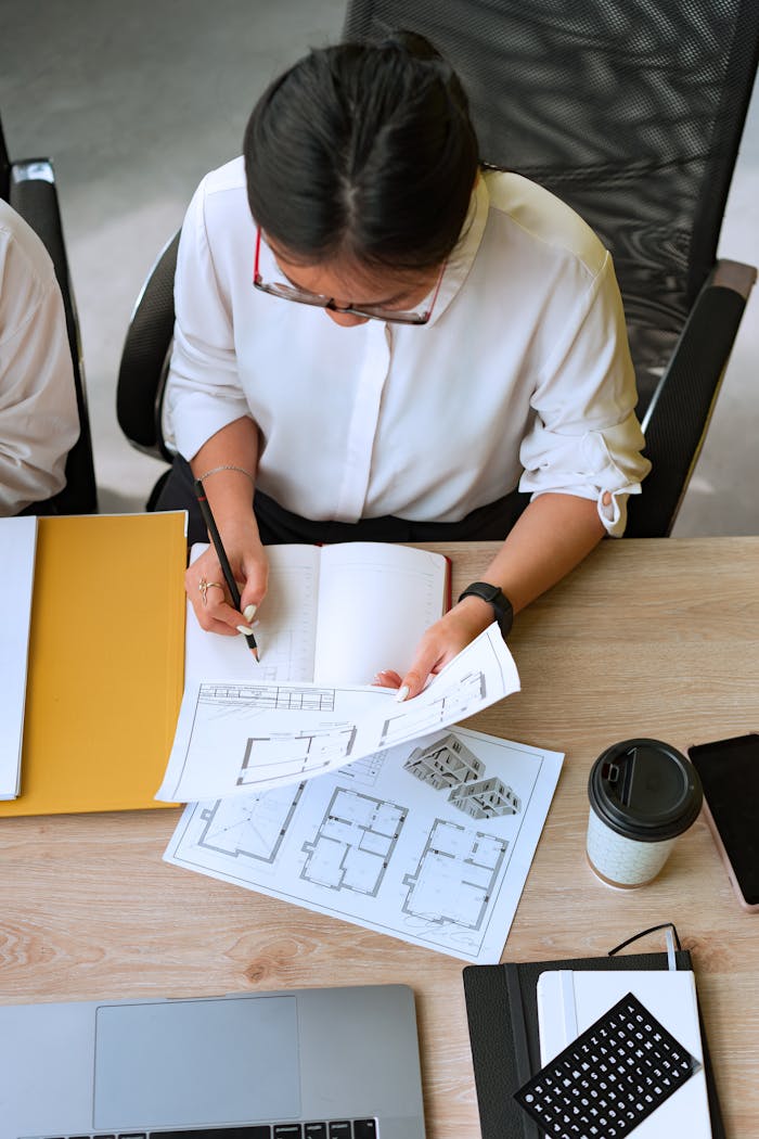 Overhead view of an architect reviewing floor plans and taking notes at a desk.